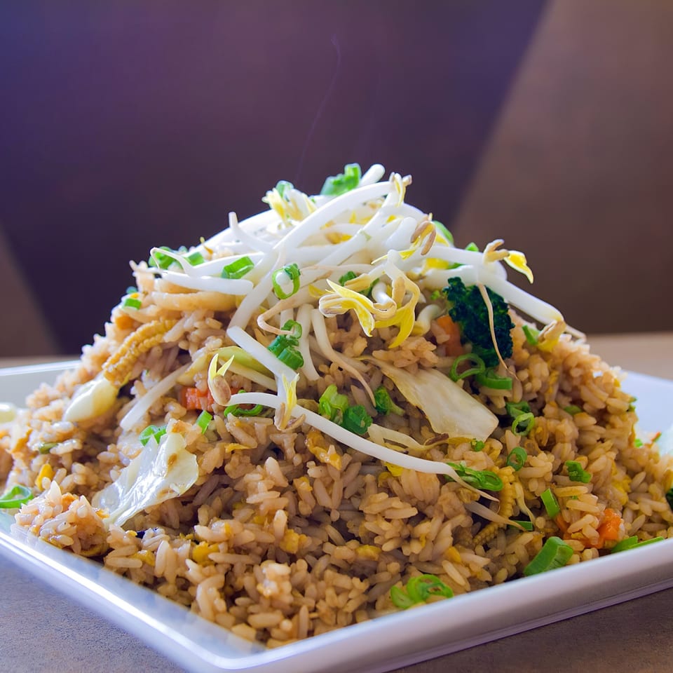 Steaming Thai fried rice with bean sprouts, green onions, and vegetables on a white plate.