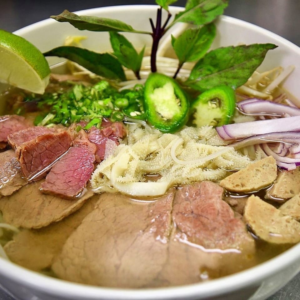 Close-up of a bowl of pho with various cuts of beef, tripe, meatballs, and fresh garnishes.
